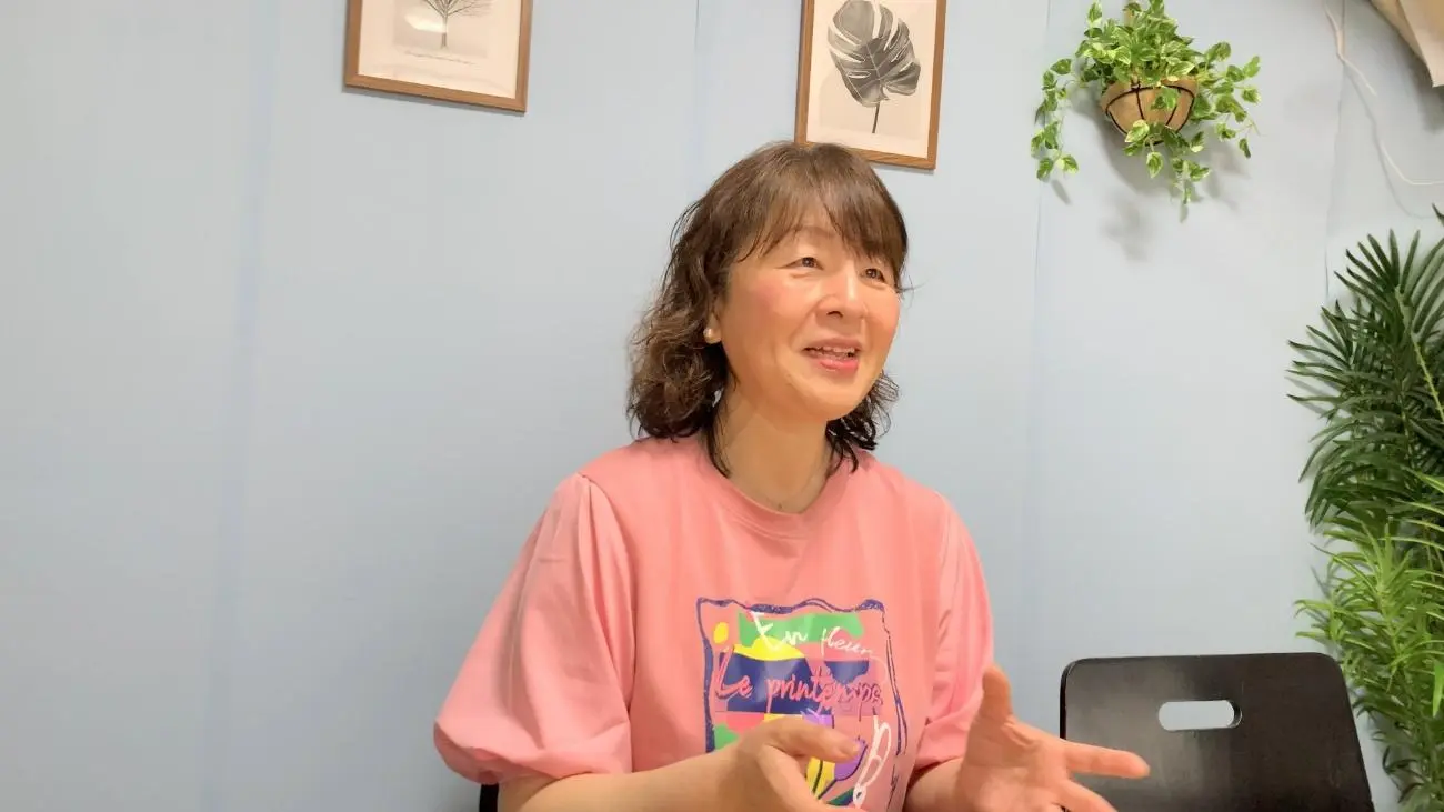 ピンクのTシャツを着た女性スタッフが手振りを交えて話している写真