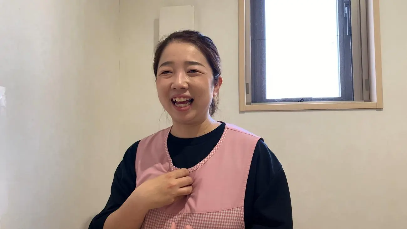 ピンクのエプロンで笑顔を見せる保育士の女性