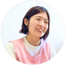 ピンクのエプロンを着た保育士が笑顔でインタビューに答えている