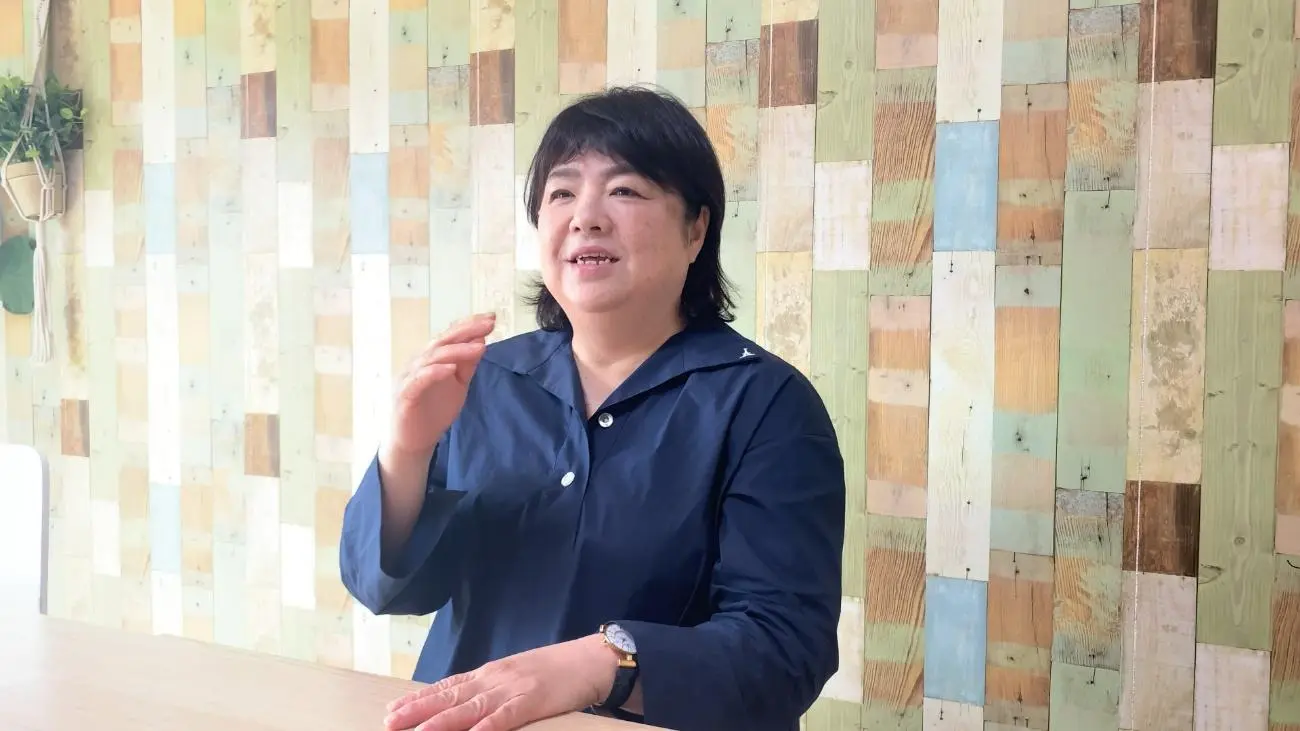 木目調の壁を背景に話す女性チームリーダーの上半身写真