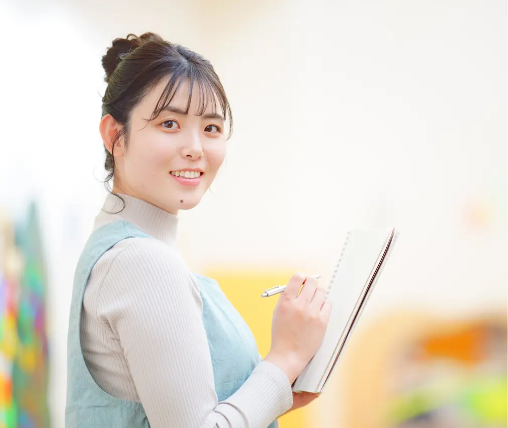 ノートを持ち笑顔を見せる女性保育士